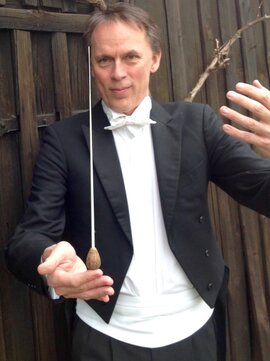 Mathias Bock balanciert in Konzertkleidung seinen Taktstock und hebt die andere Hand